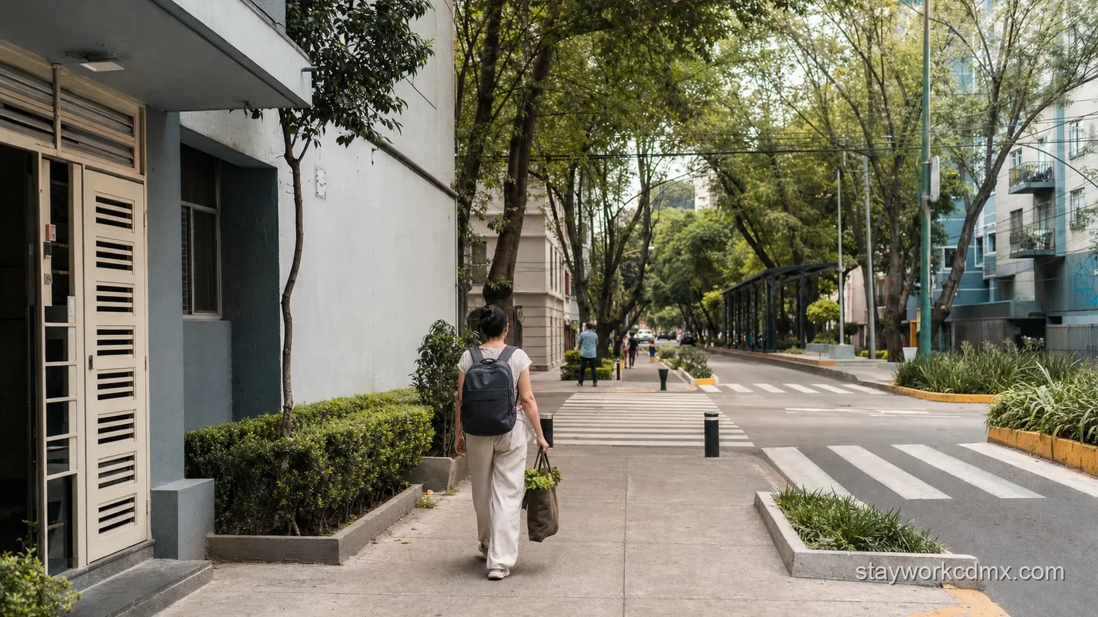 A monthly apartment guest walks from a quiet Del Valle building toward a tree-lined transit corridor, carrying a work bag and grocery tote.