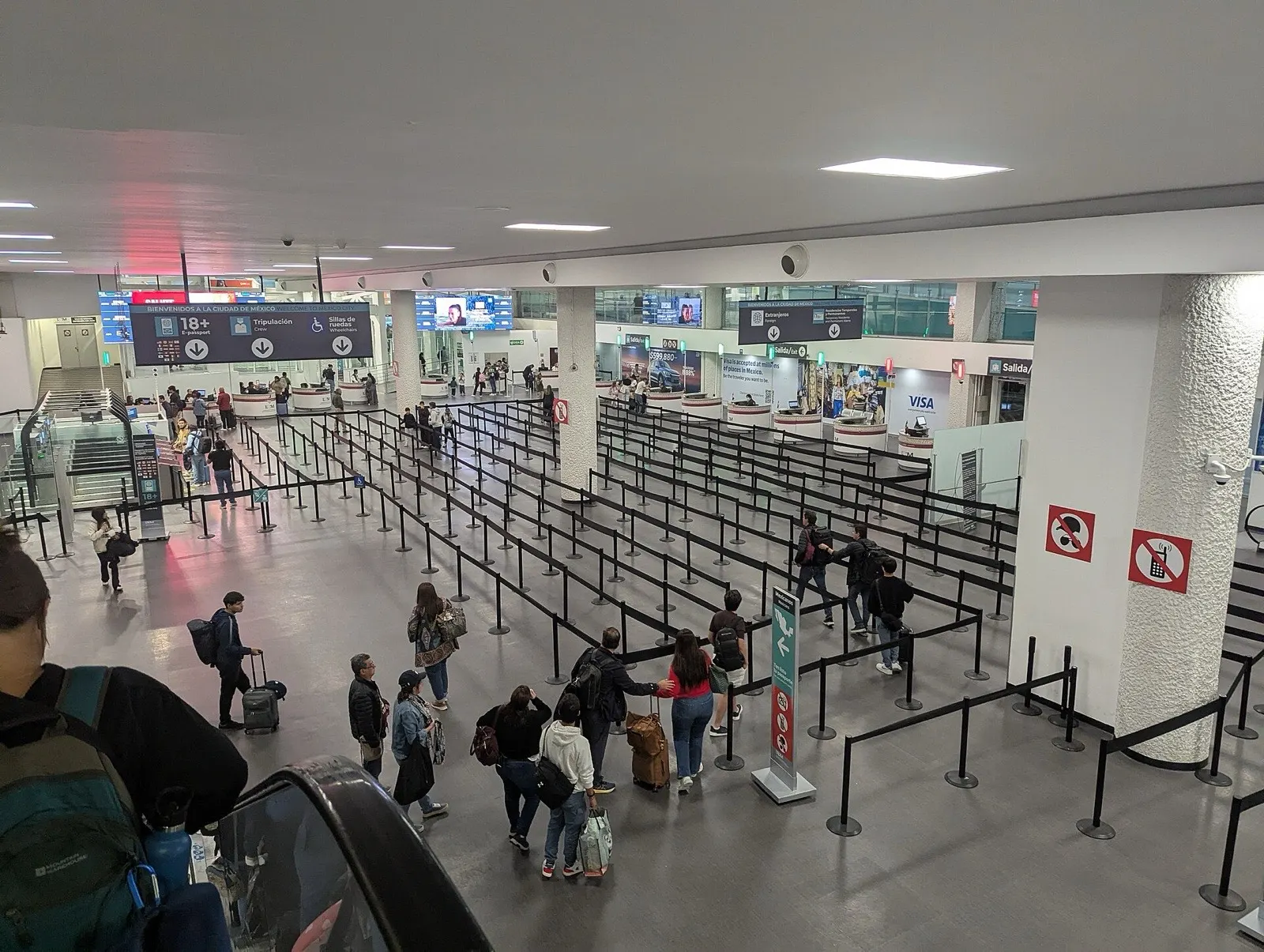 Viajeros con equipaje hacen fila bajo los letreros de migración en la sala de llegadas de la Terminal 1 del Aeropuerto Internacional de la Ciudad de México.
