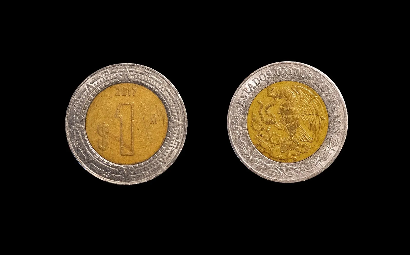 Anverso y reverso de una moneda mexicana de 1 peso de 2017, con el número 1 y el águila nacional, sobre fondo negro.