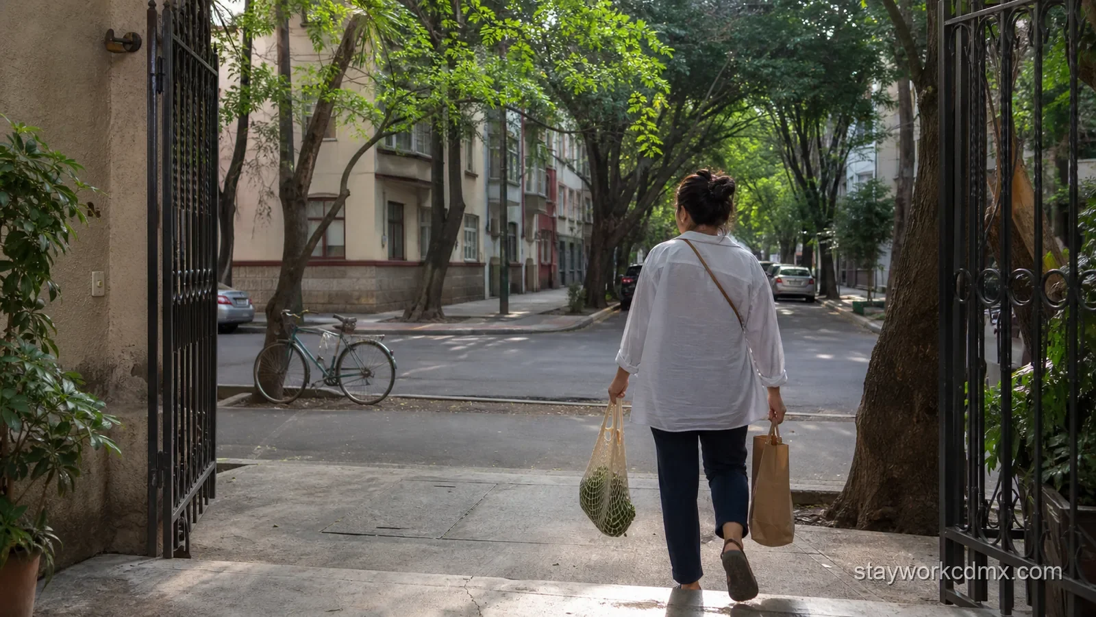 A Roma Norte resident leaves a residential apartment gate with small grocery and pharmacy bags on a shaded block.